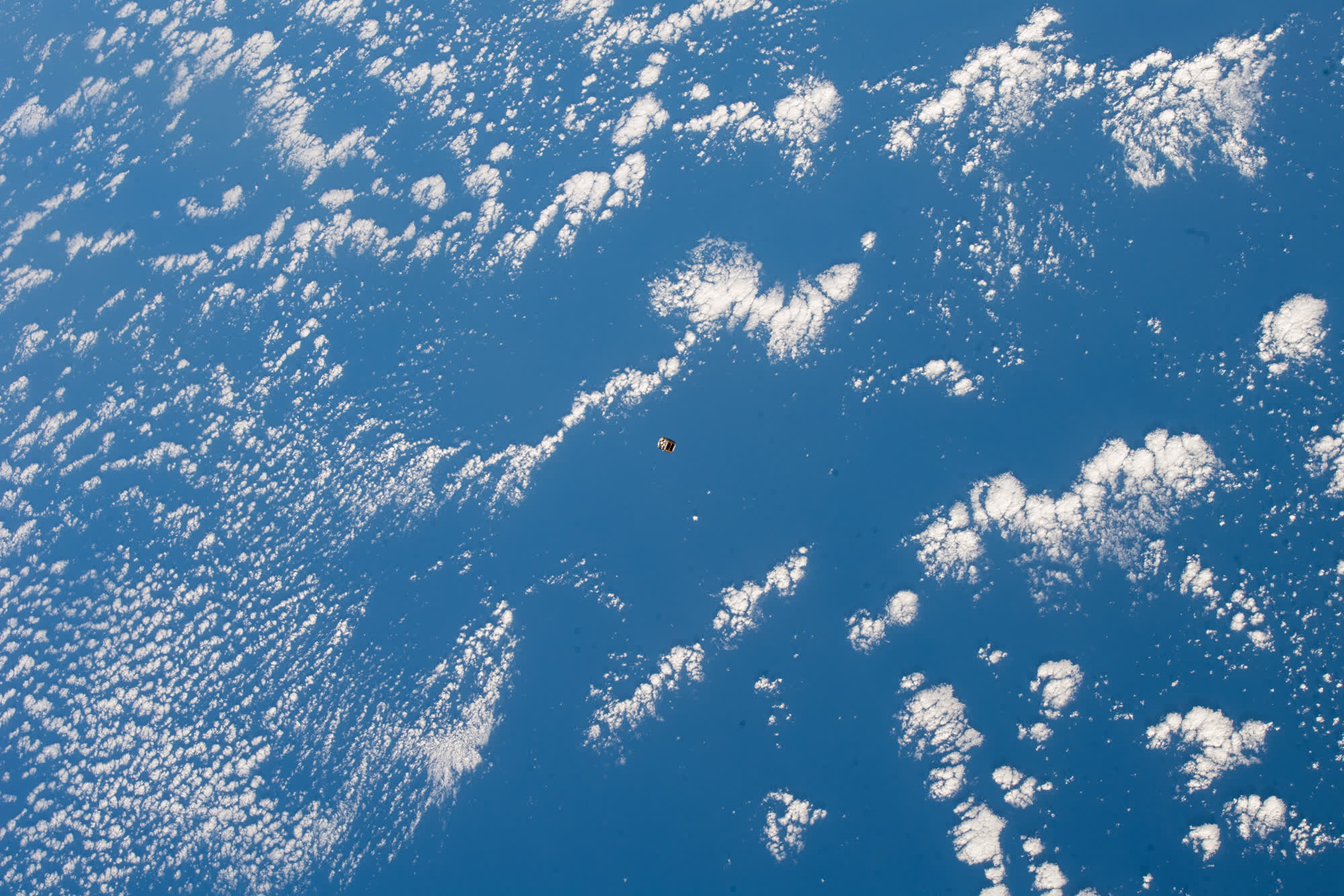 A one-unit CubeSat drifting above the Pacific Ocean and cloud cover shortly after deployment from the International Space Station
