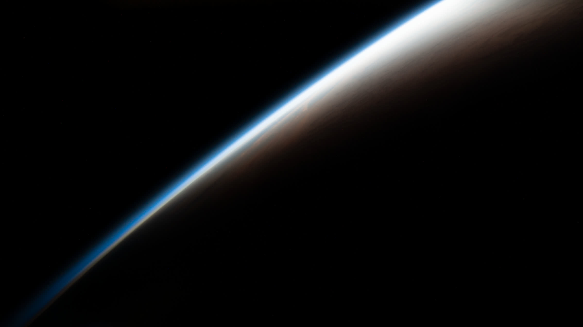 Earth's limb at orbital dawn, a thin blue line of atmosphere against black space